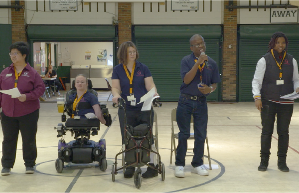 Five young adults present from a grade school gymnasium floor