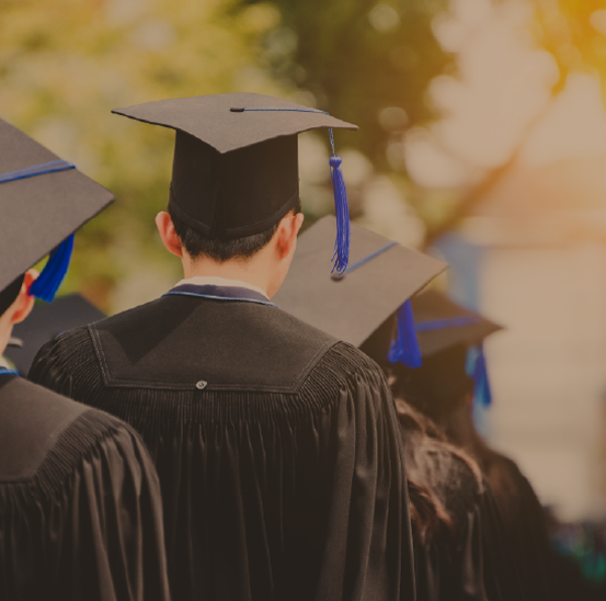 Four graduates in their cap and gowns walk away from the camera in a single file line