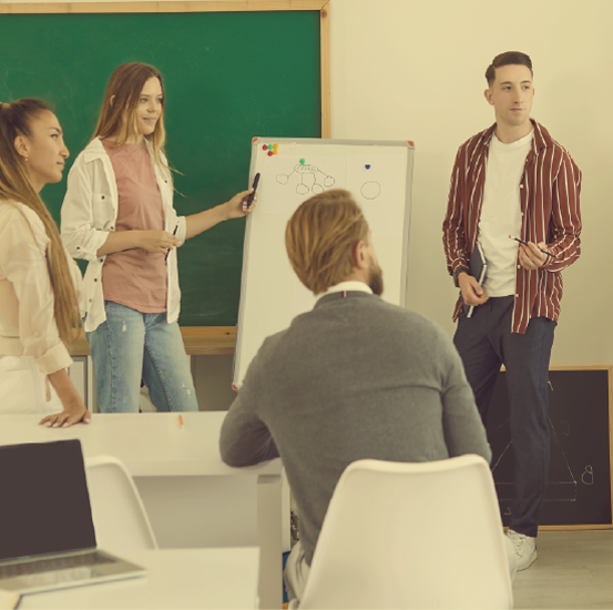 Teen stands in front of a whiteboard presenting to peers and older adult.