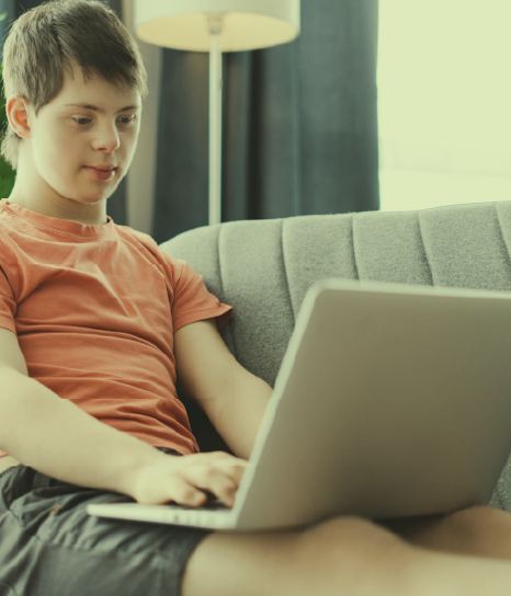 Teenage boy with down syndrome is sitting on a couch, using a laptop